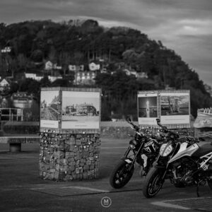 Two motorcycles parked by a historic display in Minehead.