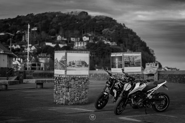 Two motorcycles parked by a historic display in Minehead.