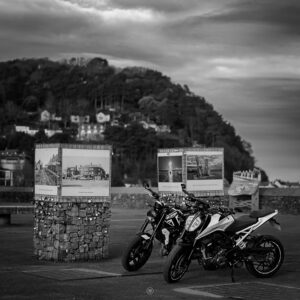 Two motorcycles parked by a historic display in Minehead.